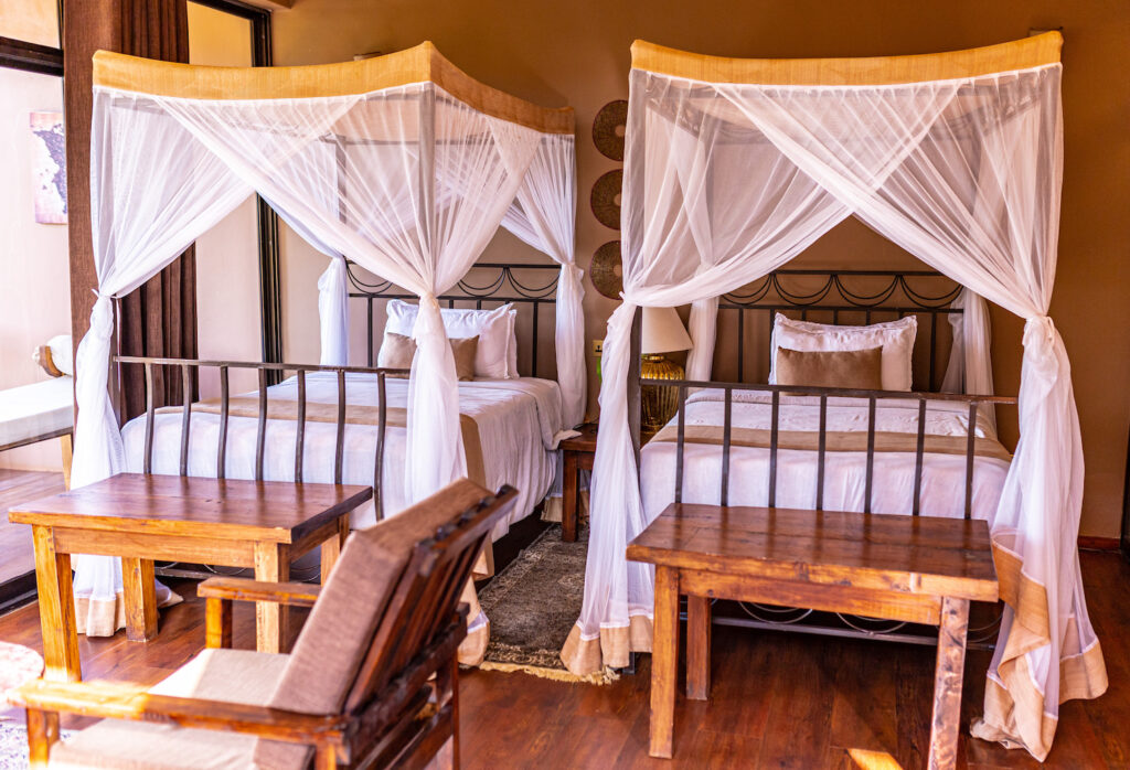 Interior of a cozy bedroom at Highview Coffee Lodge in Tanzania, featuring two queen beds with white canopy mosquito nets and wooden furniture.